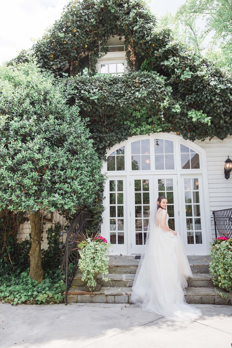 A bride in a wedding dress standing in front of a house with ivy at Cedar Weddings and Events