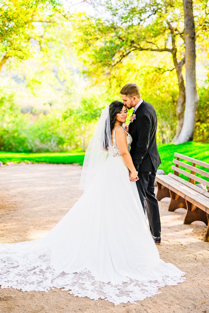 groom kissing bride's forehead with greenery and trees at Van Dickson Ranch Skull Valley Prescott