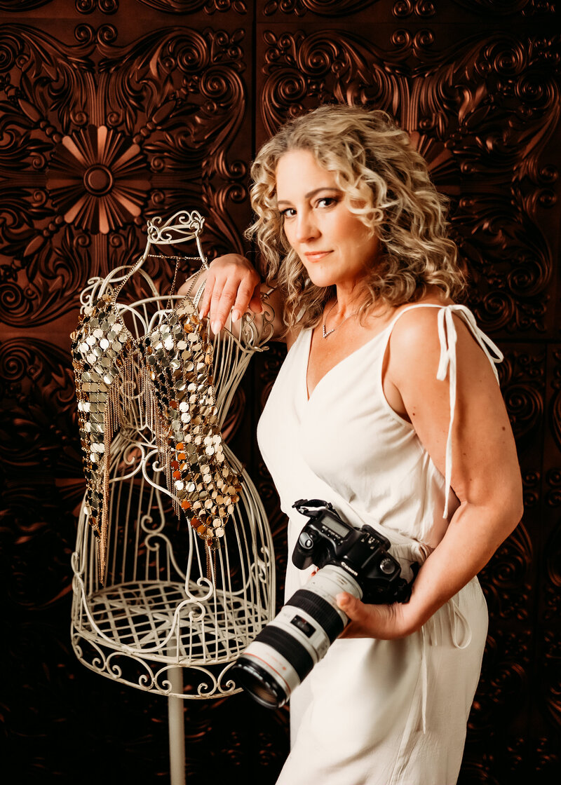 woman boudoir photographer with curly hair wearing a brown leather jacket holding her canon camera