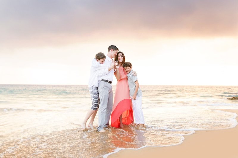 Family of four smiles on the beach for a family photo in Big Island Hawaii