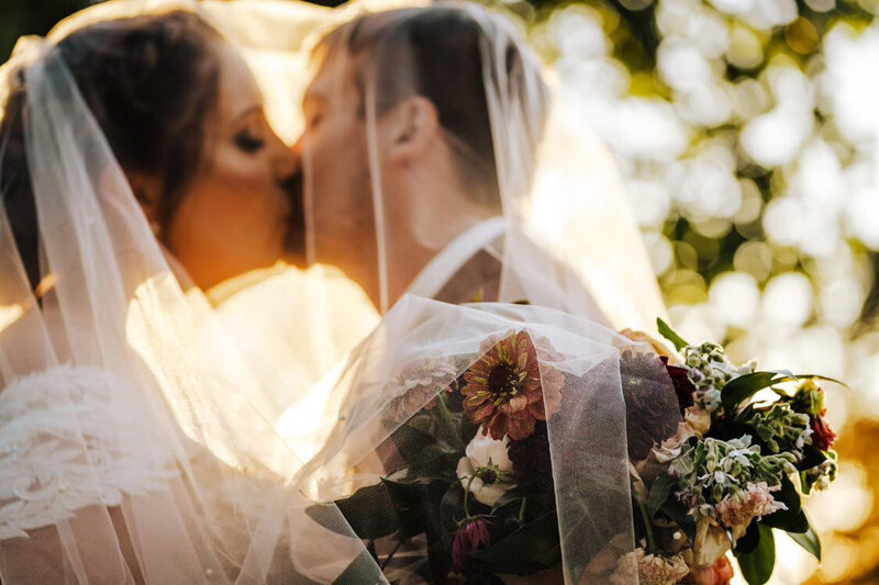 bride and groom posed under her custom pearl bridal veil blusher during golden hour