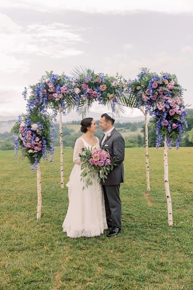 Bride and groom embrace beneath a floral chuppah