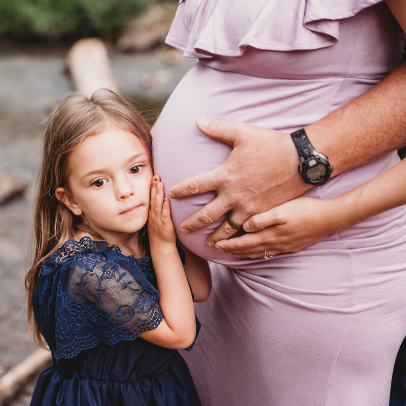 Young girl listening to her mom's pregnant belly