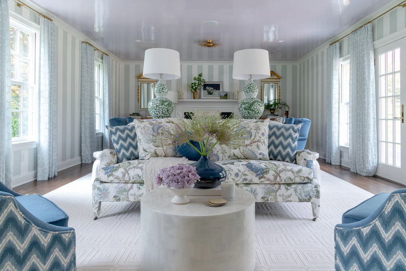 Living room interior featuring a floral upholstered settee, green chinoiserie table lamps, circular marble coffee table and two blue toned ikat chairs in the forefront.