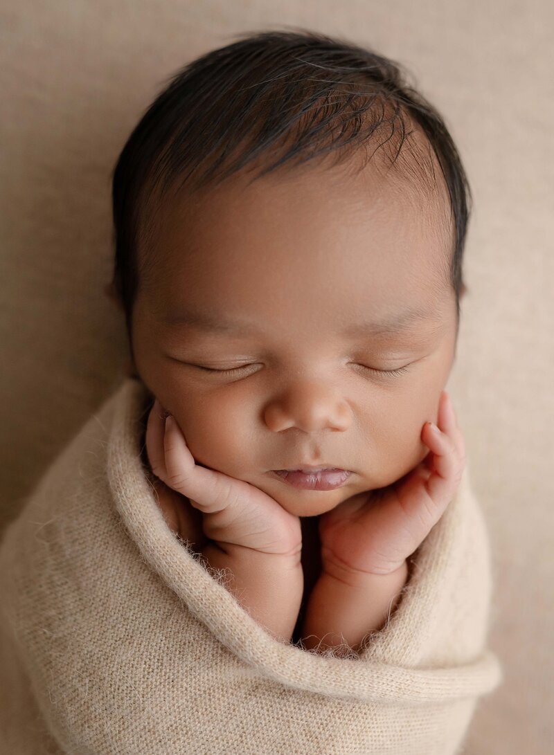 Baby boy swaddled in cream wrap, sleeping, with his hand on his cheeks. Photo was taken by Jenni Nikki at her Marietta studio near Atlanta GA