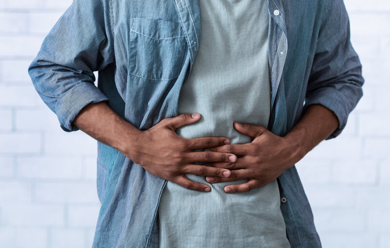 Male with blue and green shirt holding stomach in pain