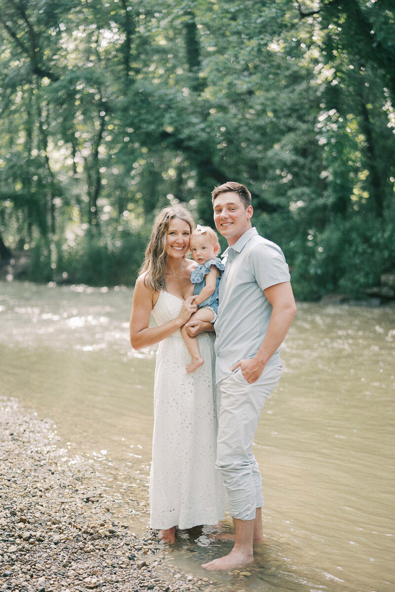 parents holding daughter near creek
