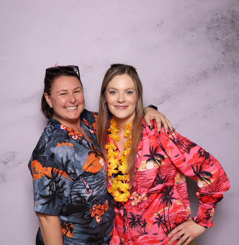 Two women smiling joyously in Always Present photo booth with minimal backdrop