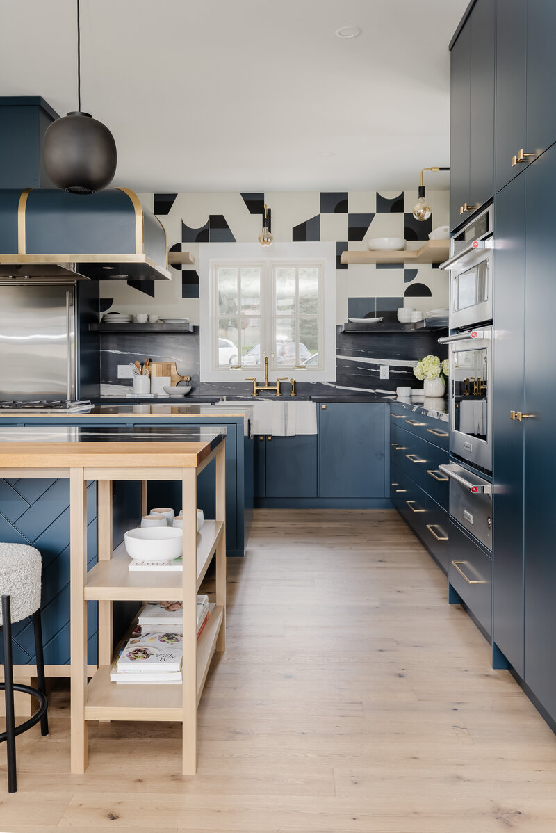 A kitchen walkway showcasing wood flooring, deep blue cabinetry with brass accents, and an abstract black and white wall mural