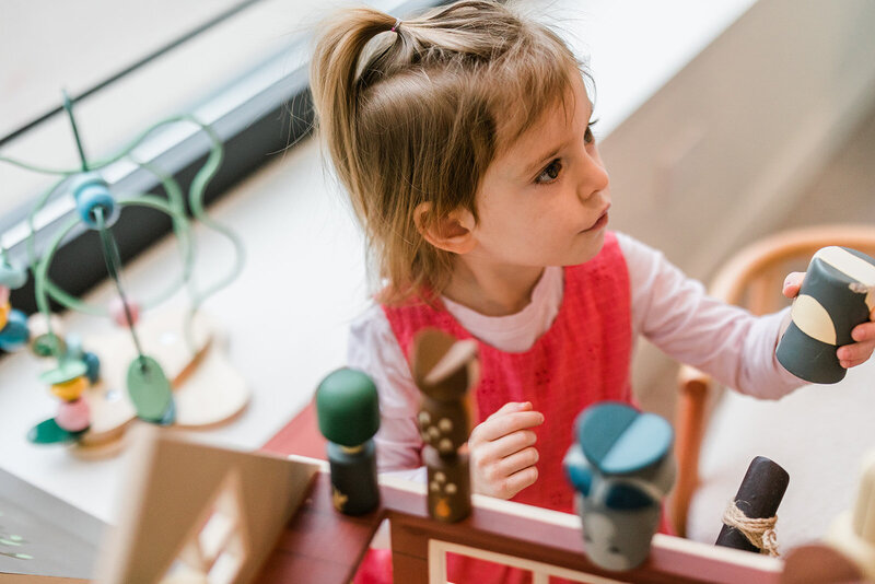 A little girl with part of her toddler hair gathered into a ponytail, plays with classic wooden toys in the waiting area of Andersonville family dentist, Michael Rabinowitz, formerly of Growing Smiles.