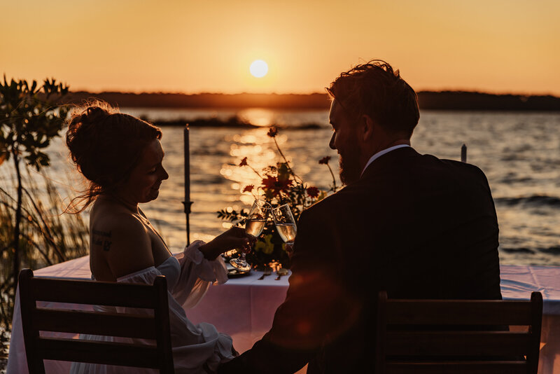 Shannon Lee, a Florida elopement photographer capturing a romantic sunset toast between a couple sitting by the water.