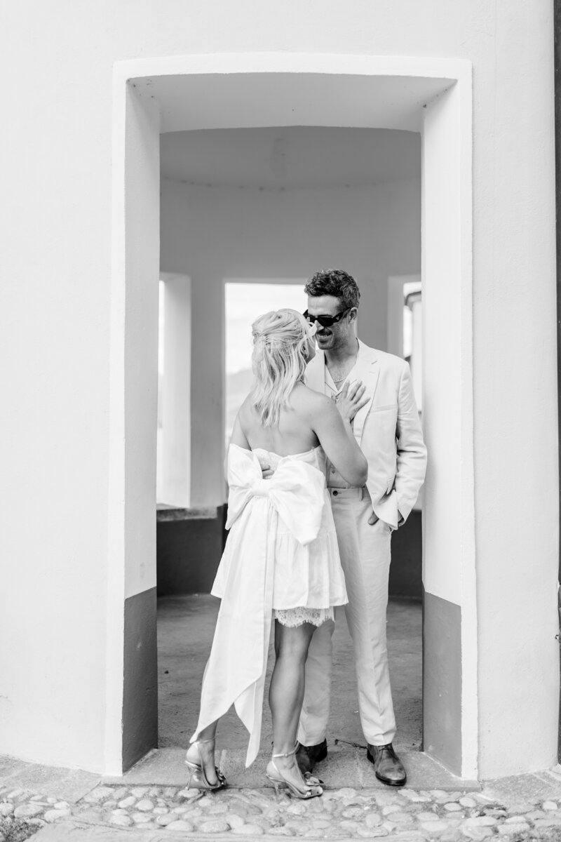 Couple in Lake como that is standing next to a door opening and the bride has a big bow on her dress
