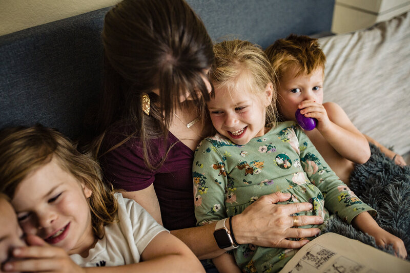 mom cuddles and reads to her four kids on her bed.