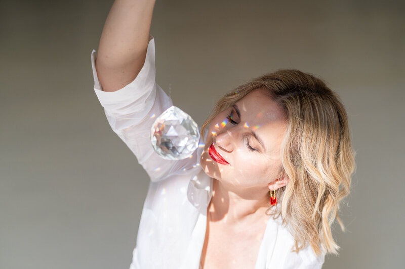 žena v bílých šatech drží před sebou skleněnou kouli s vybroušenými hranami a má zavřené oči