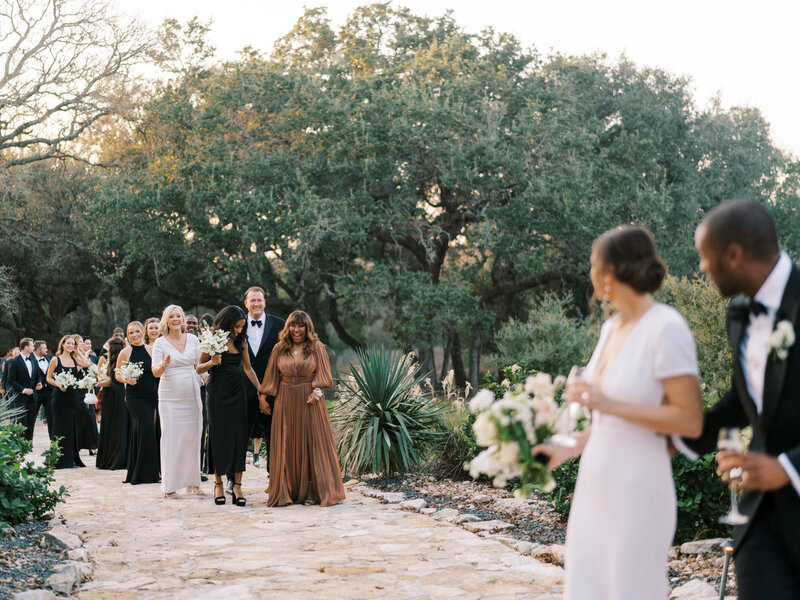 In focus bridal party and family walking towards out of focus bride and groom