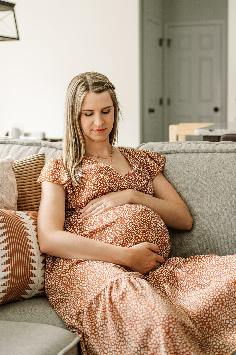 pregnant mother in and orange dress sitting and holding belly by york pa photographer