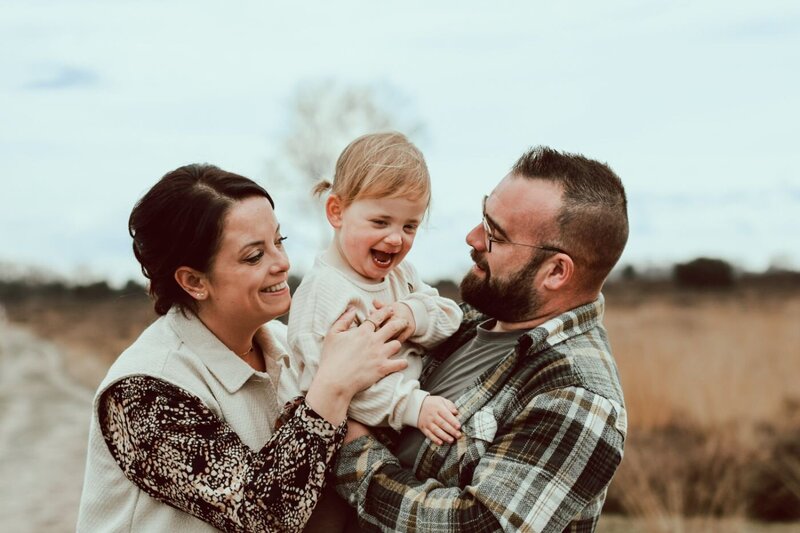 Een vrolijke familiefoto van ouders met hun jonge kind in een natuurlijke omgeving.