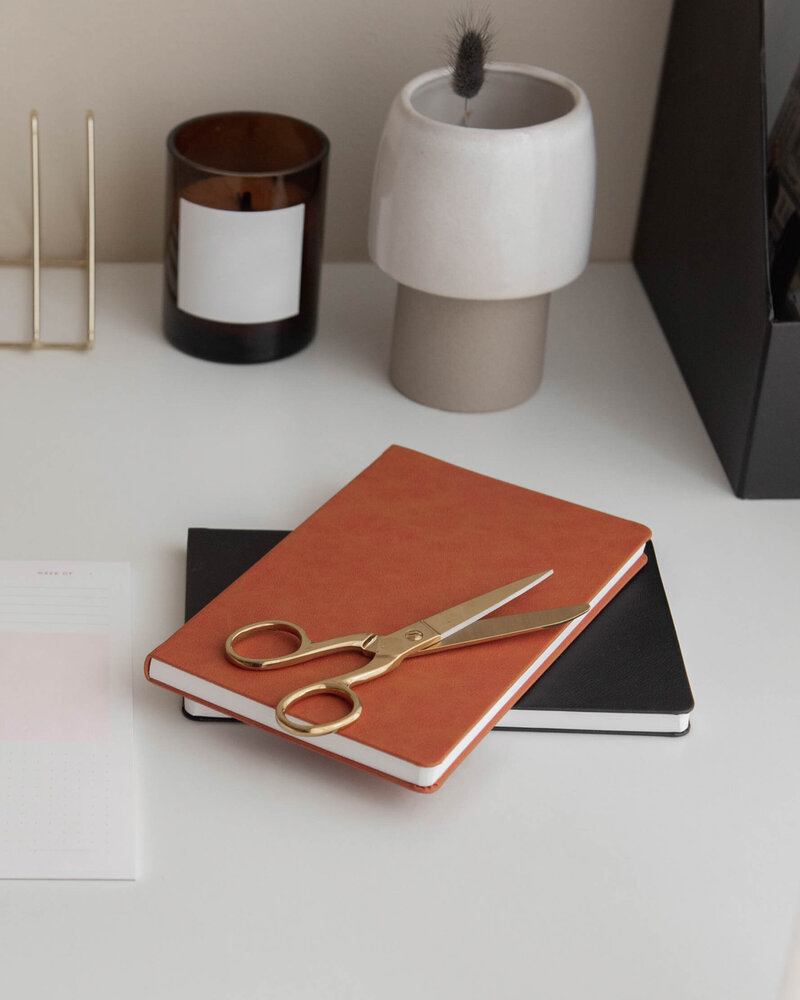a stack of notebooks on a white table. there is a pen on the top notebook