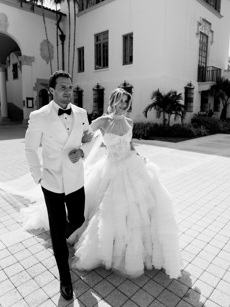 Bride in custom Monique Lhuillier wedding gown walks with groom at their wedding in Miami, FL
