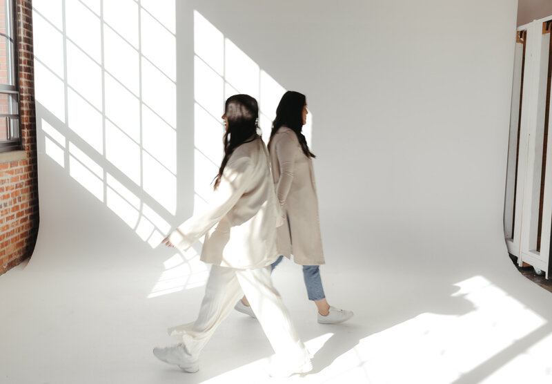 Two members of the Riviera Creative team walking sideways by each other in front of the camera wearing cream and blue jeans