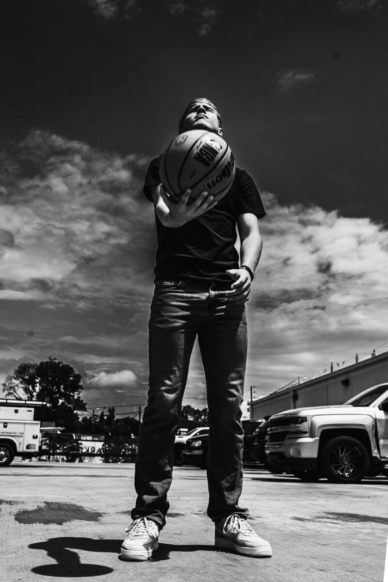 Black and white image of a boy looking up at the sky holding a basketball.  
