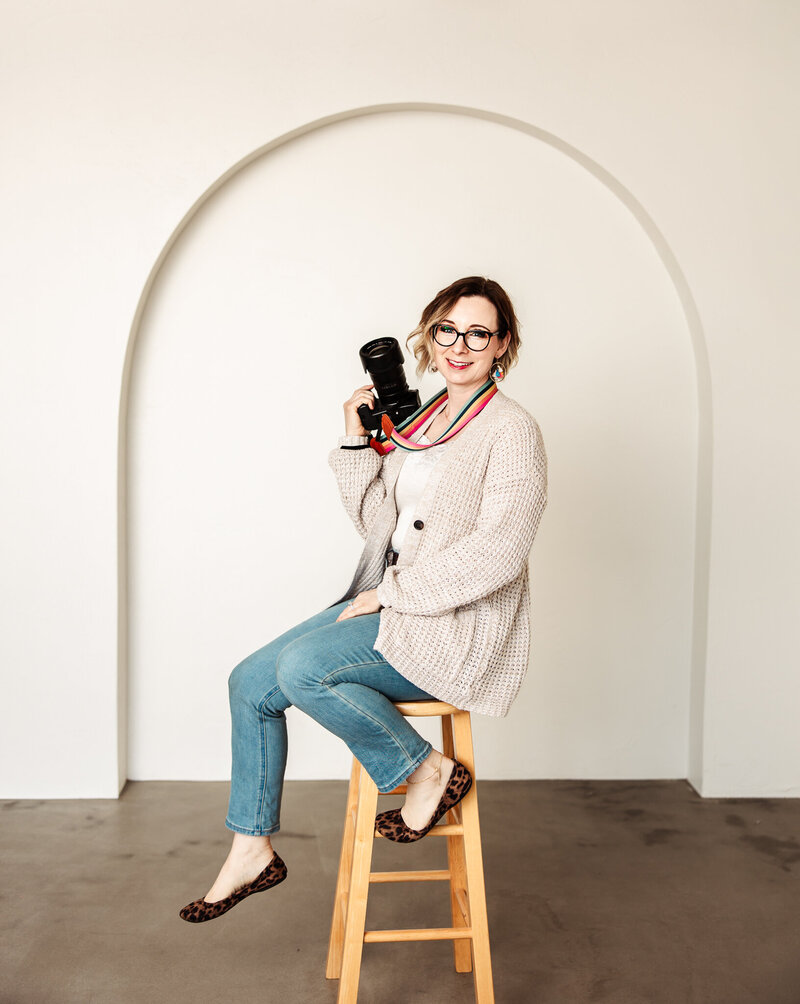A photographer sits on a rock with legs crossed and smiling at the camera