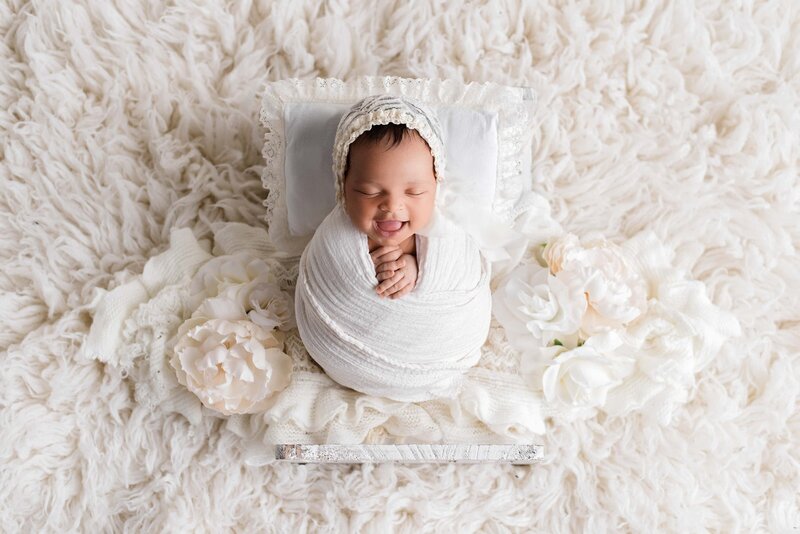 Newborn baby girl wrapped and smiling on prop bed in white and cream
