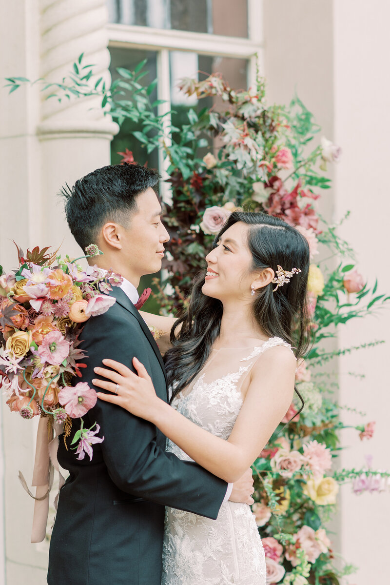 16-alisonbrynn-Radiant-LoveEvents-Maxwell-1-House-bride-groom-holding-eachother-smiling-in-alter-floral-column-backdrop-outdoors-romantic-elegant-timeless