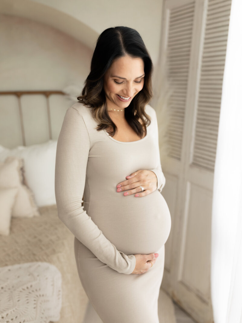 pregnant mother in beige maternity gown holding baby bump for maternity photos Cleveland family photographer