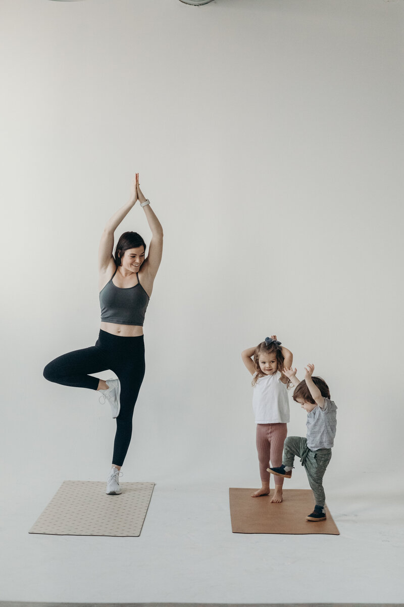 Good For The Swole Founder, Becky Burgess, does yoga tree pose along her two young chuldren