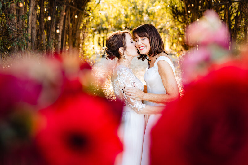 A wedding couple hugging and kissing in the gardens at Zingermans Cornman Farms in Dexter Michigan surrounded by red flowers and warm gardens