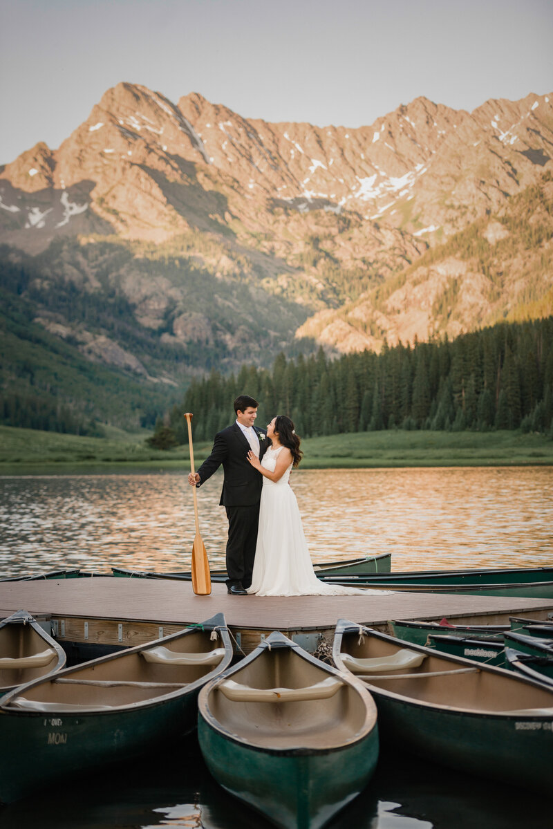 Groom and Bride standing on a dock holding a canoe paddle