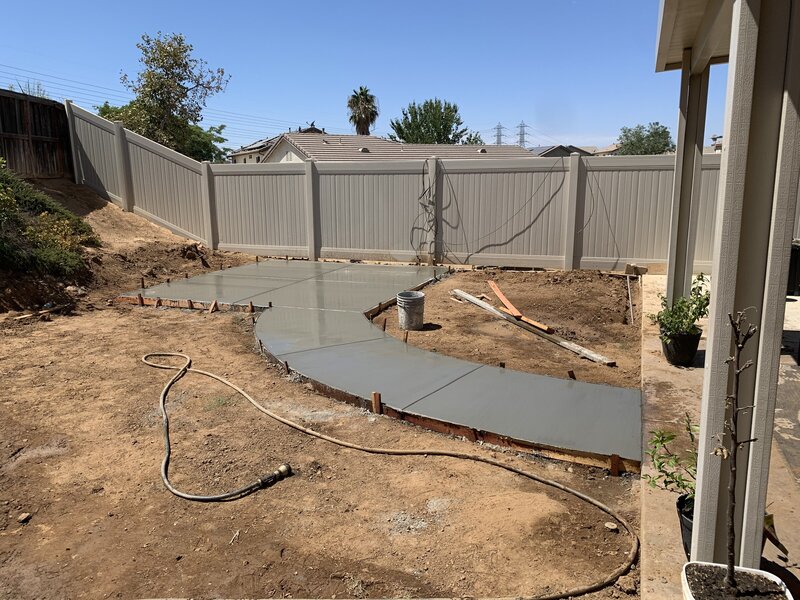 A backyard with dirt and a fresh poured cement path leading to a cement pad.
