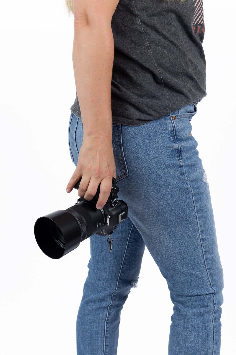 Close up of Megan holding a camera while wearing jeans and a casual grey shirt | Senior Photographer in Lawrence, KS