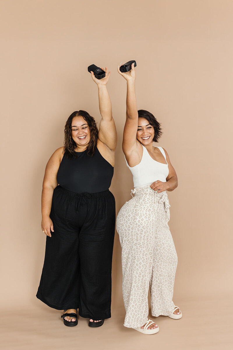 wo hosts of a self-love podcast posing joyfully with microphones in a minimalist studio during a personal branding photoshoot.