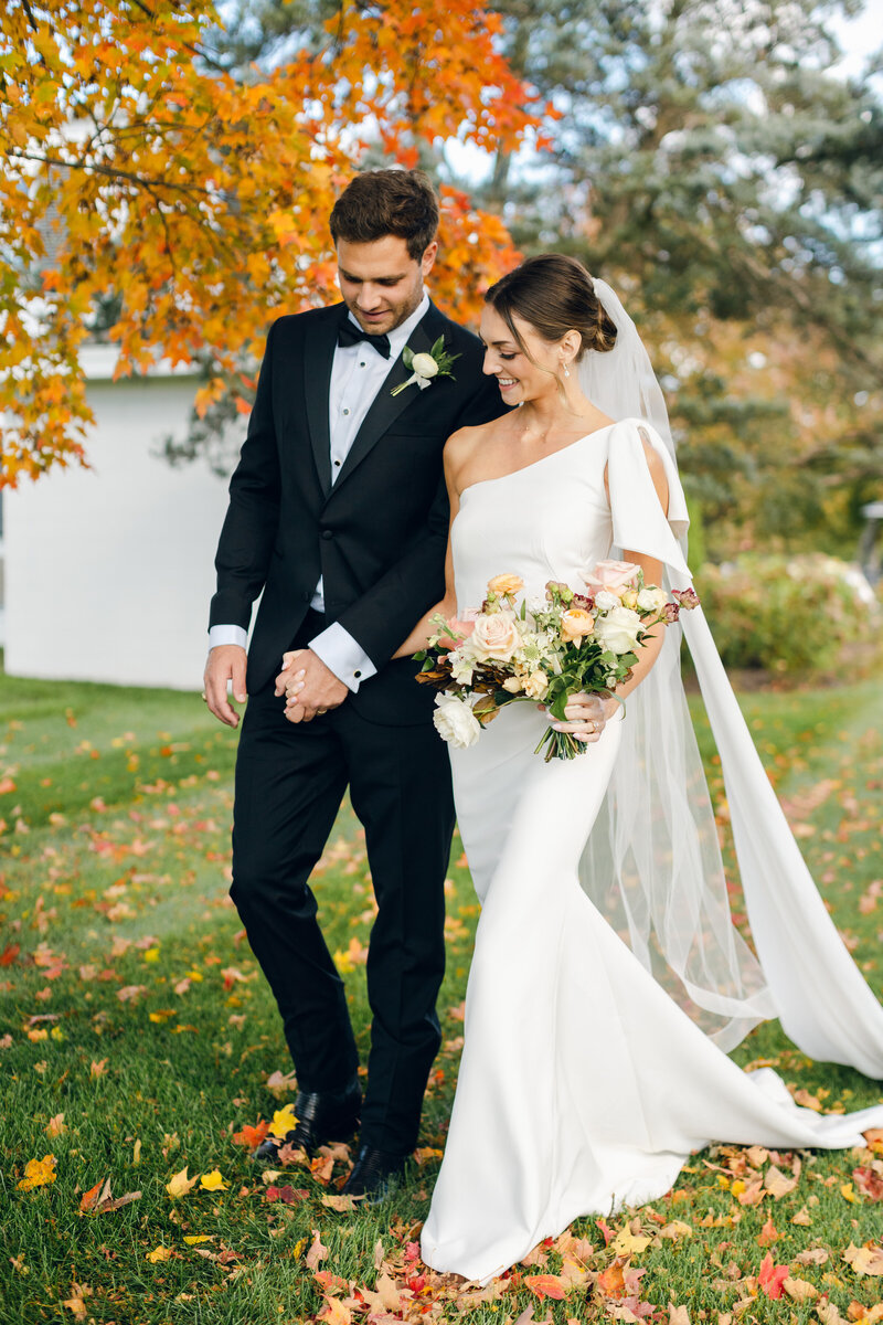Wedding couple embracing in sunlit garden setting with peach and white bouquet.