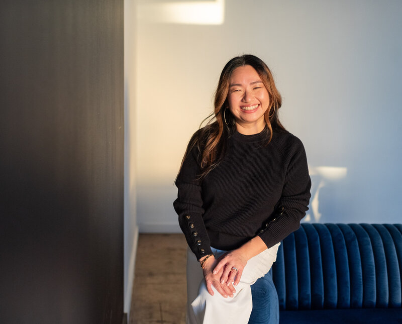 An Asian woman sitting on blue velvet couch with a smile.