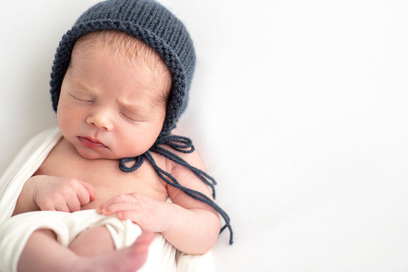 a sweet sleeping baby partially swaddled and wearing a blue knit hat taken by Bucks County Newborn Photographers Ivory Tree Portraits