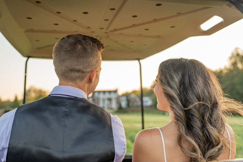 Bride and groom riding in a golf cart toward a private estate near Montpelier, VA, during their wedding day, bathed in golden hour light