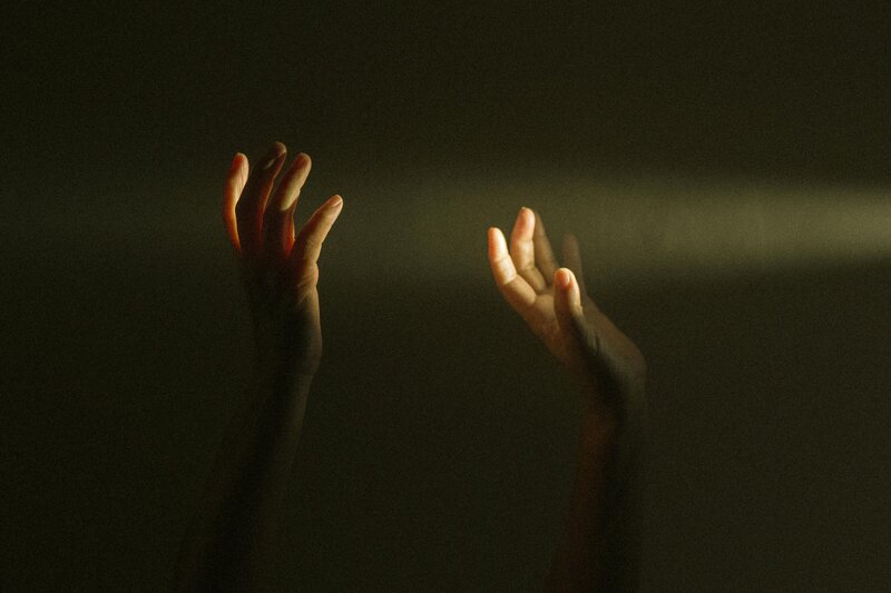 Image of hands raised to touch ray of light in dark room