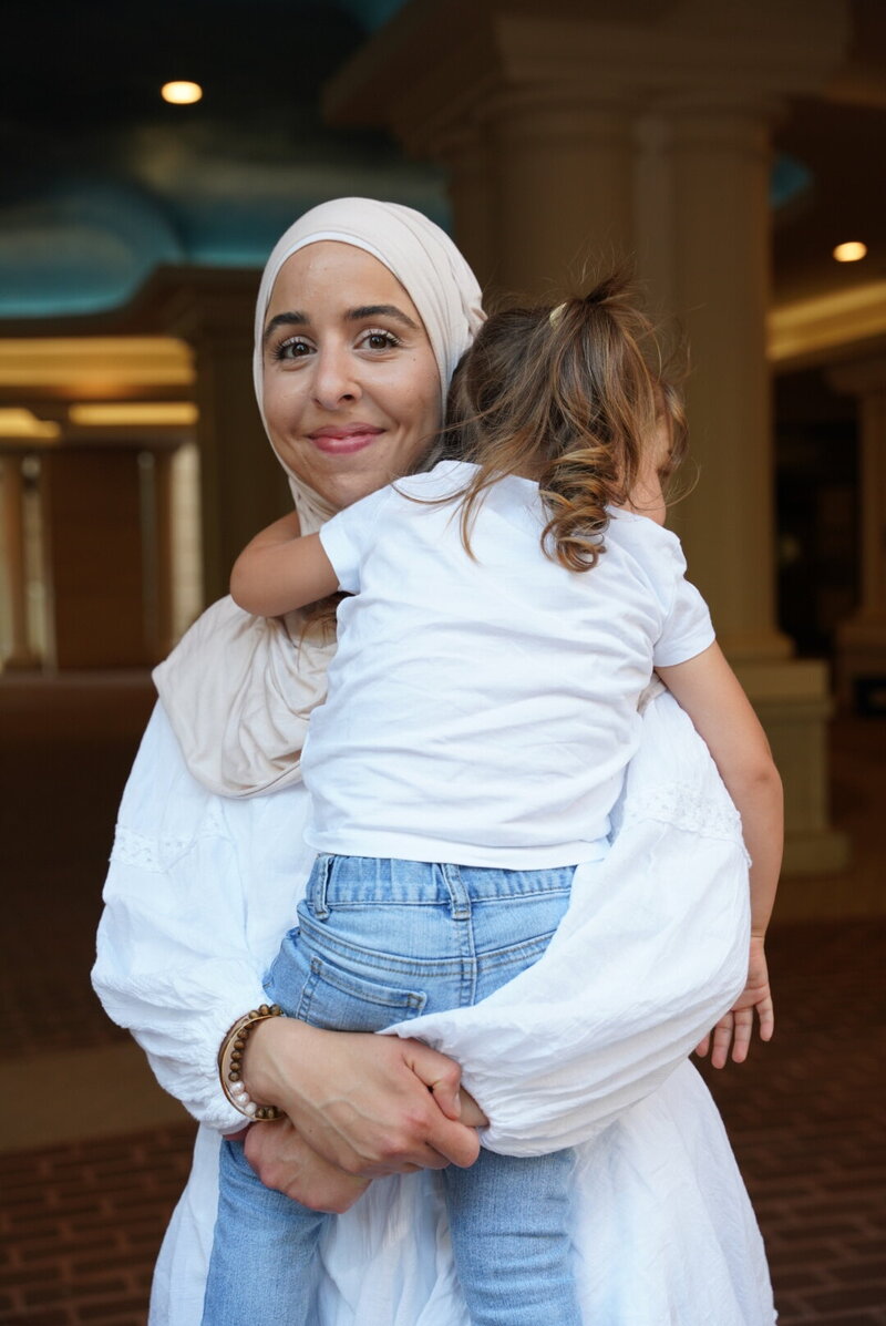 Fitness hijabi coach Hanan posing with a smile while holding her toddler daughter