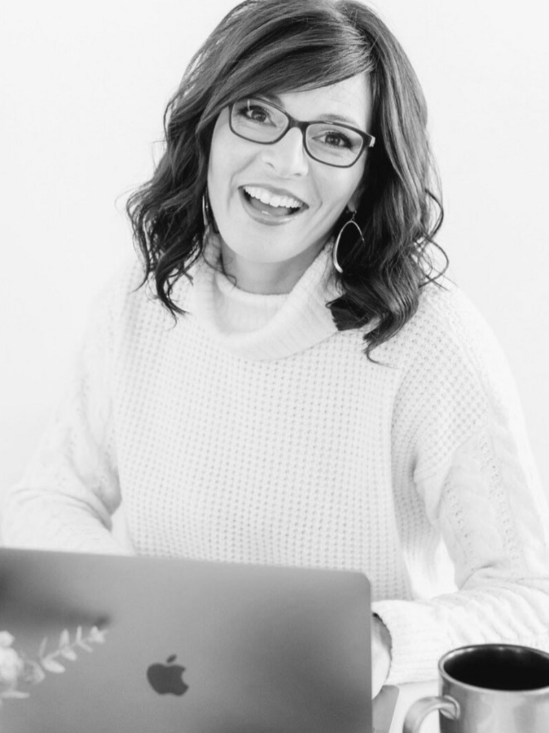 woman with dark hair and glasses black and white image smiling at camera sitting in front of laptop