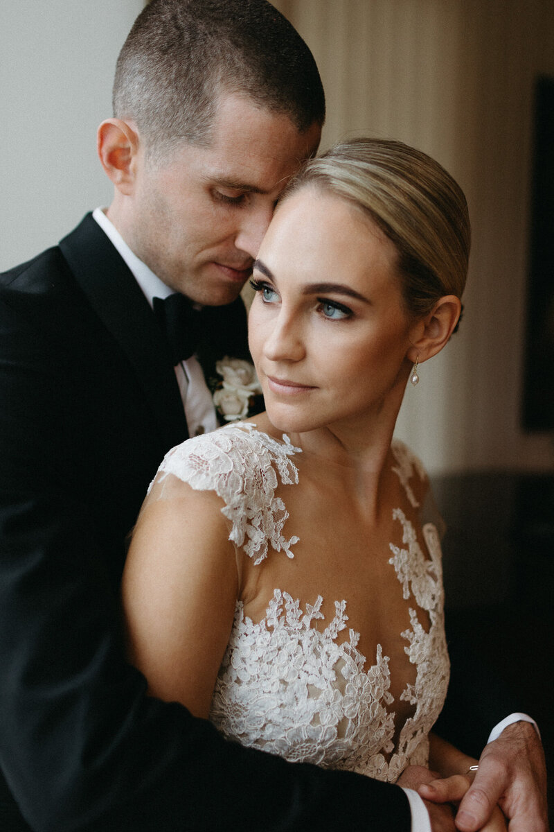 Groom nuzzles into the neck of a beautiful bride in a lace wedding gown inside the Cape, a venue in Prince Edward County. Photographed by PEC wedding photographer Jennifer van Son