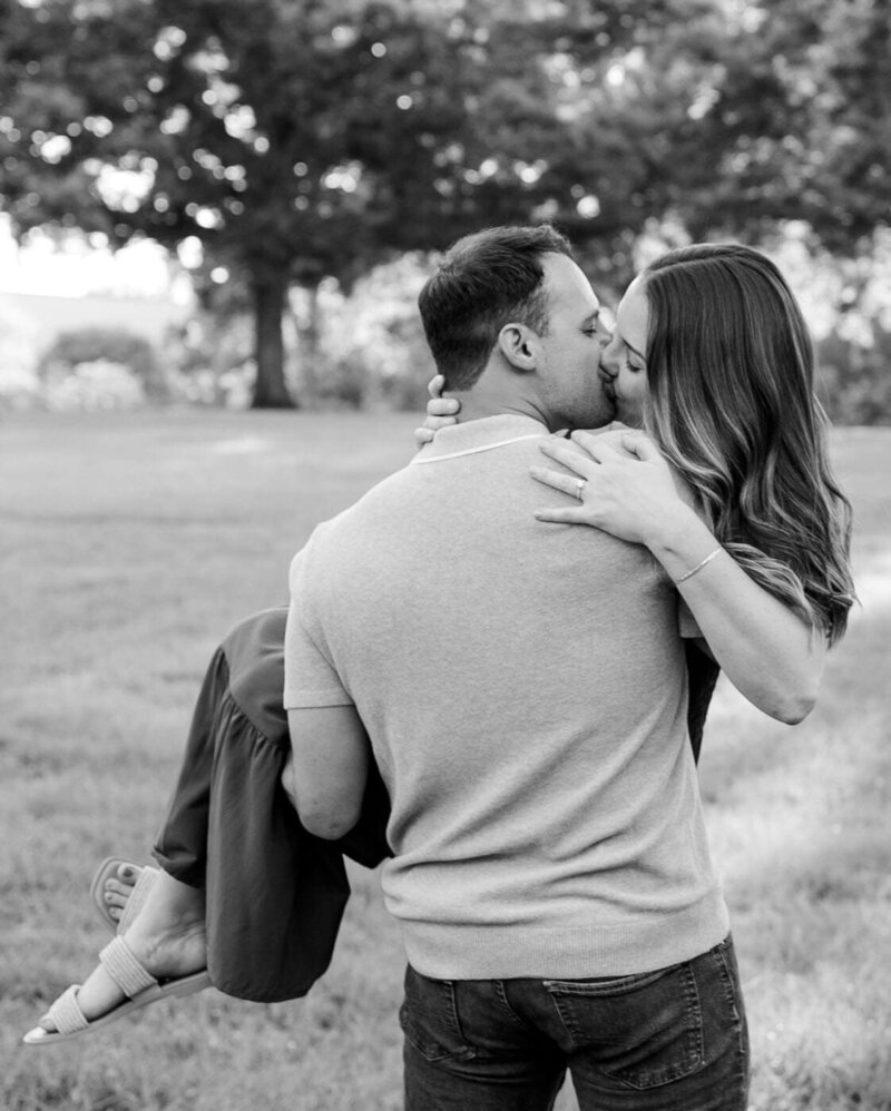An engaged couple sharing a kiss as he holds her. 