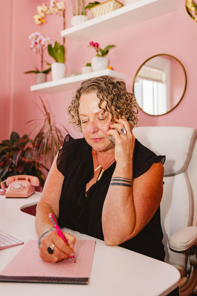 Oregon business lawyer Cassie holds a phone to her ear and takes notes while sitting at her next.