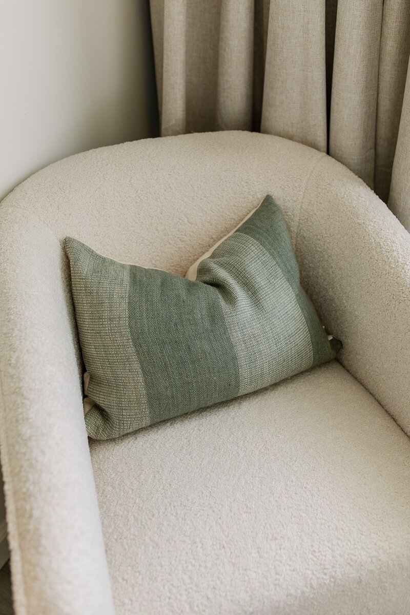 Bedroom study corner with fluffy cream chair, rust pillow, gold lamp, and foot cushion in Encinitas, California.