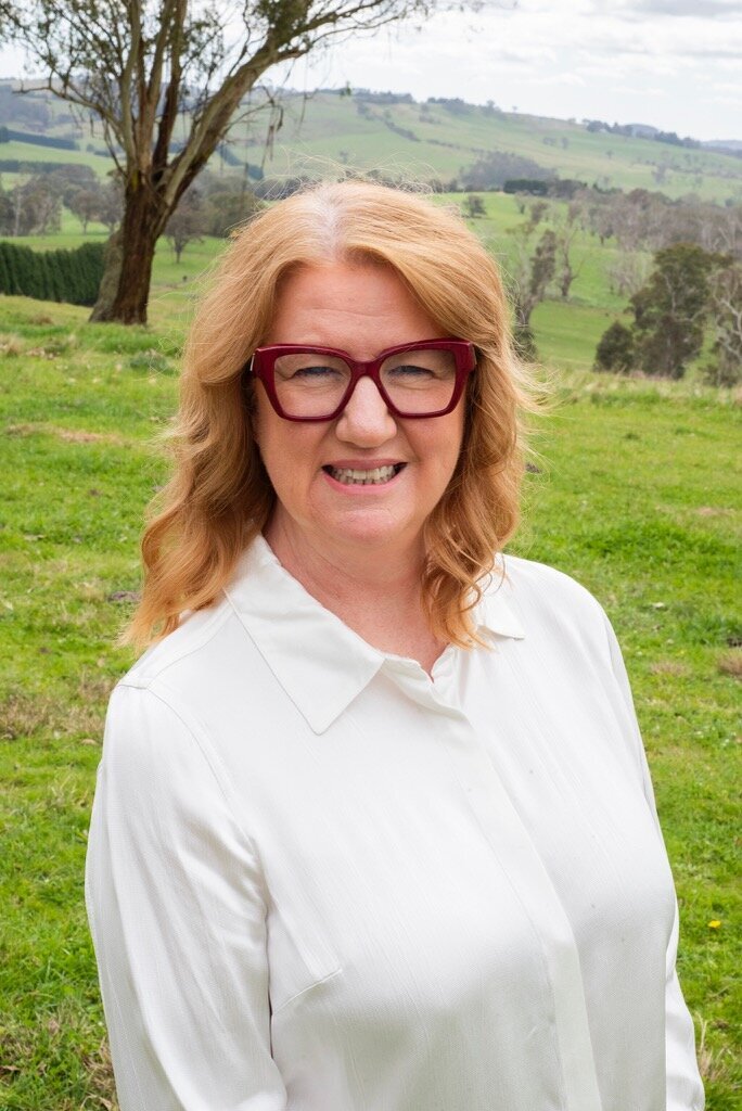 Suzanne Harrison wearing a white shirt with red glasses in a green field 