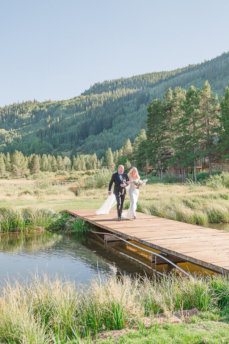 Dad walks the bride across a bridge to meet her groom in epic mountain wedding venue.