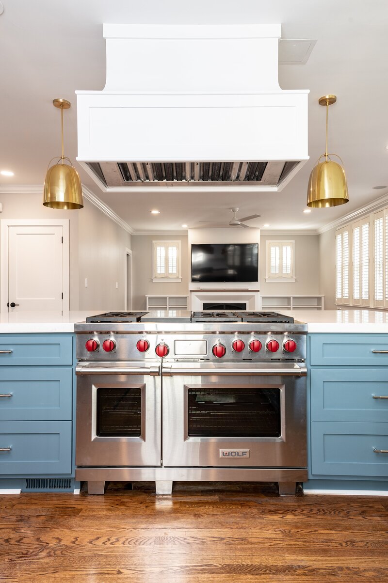 High-end kitchen featuring blue cabinets, gold hardware, a professional-grade stainless steel stove, and white subway tile backsplash