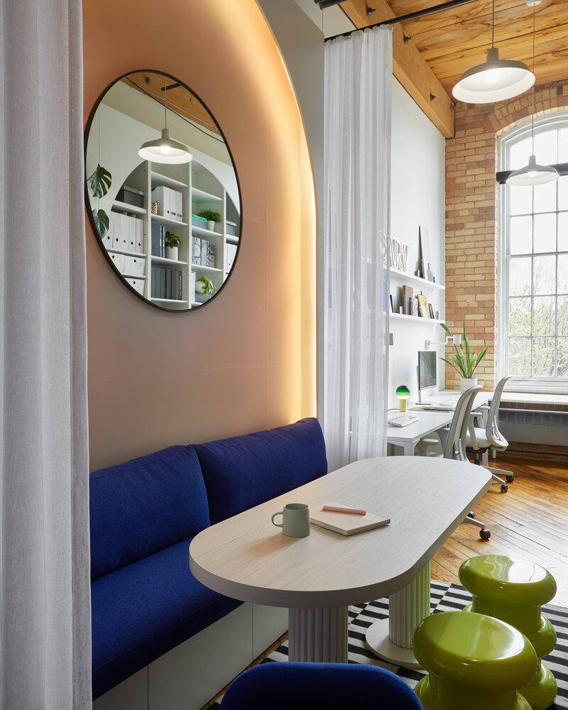 A meeting area featuring an elegant wood table surrounded by stylish blue and green seating, with soft warm backlighting and round wall-mounted mirror.